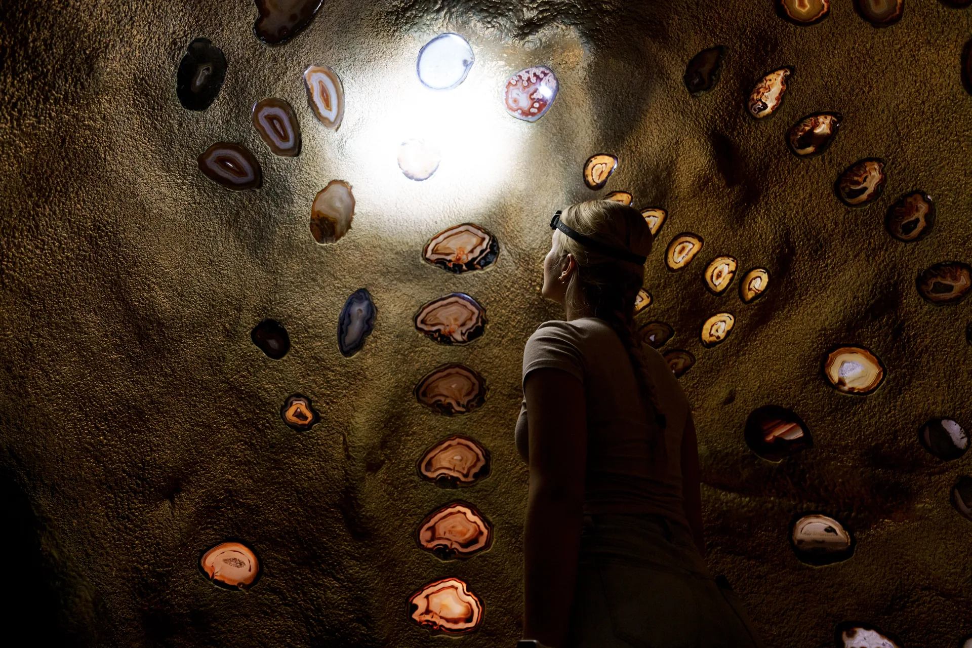 A visitor admires a cave wall studded with backlit polished agate slices at Crystal Caves
