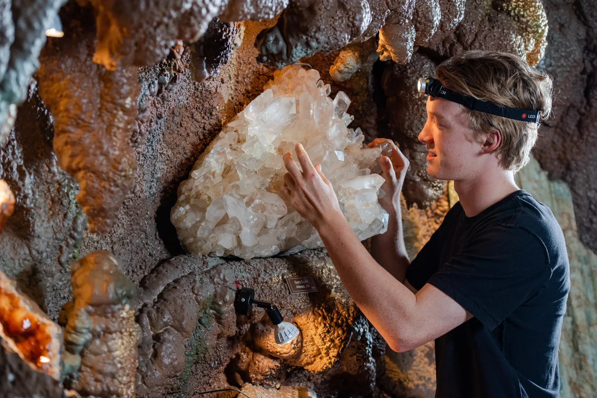A young visitor touches a white quartz crystal cluster embedded in the cave wall at Crystal Caves