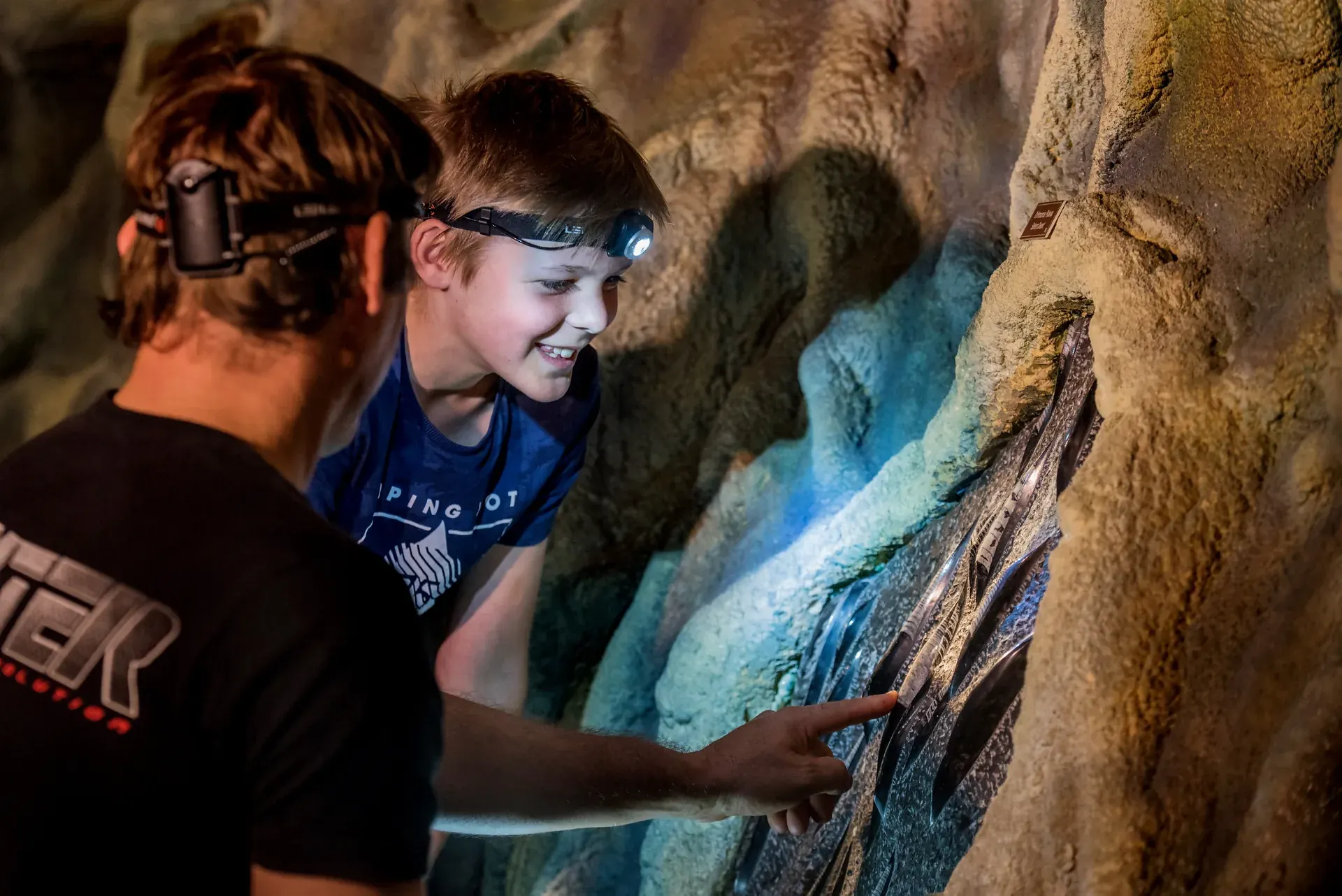 A father and son wearing headlamps touch an illuminated rock formation at Crystal Caves